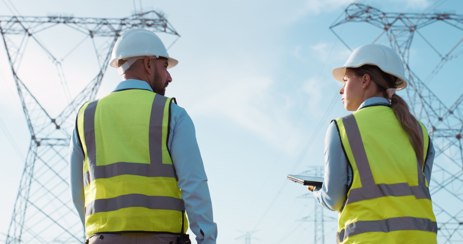 Teamwork, electrical engineer and construction in power station with tablet for electricity inspection and tower check. Engineering, rear view or collaboration for energy distribution and maintenance